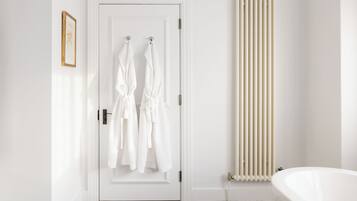 A bathroom with a white door, two white towels hanging on hooks, a white radiator, and a white bathtub.