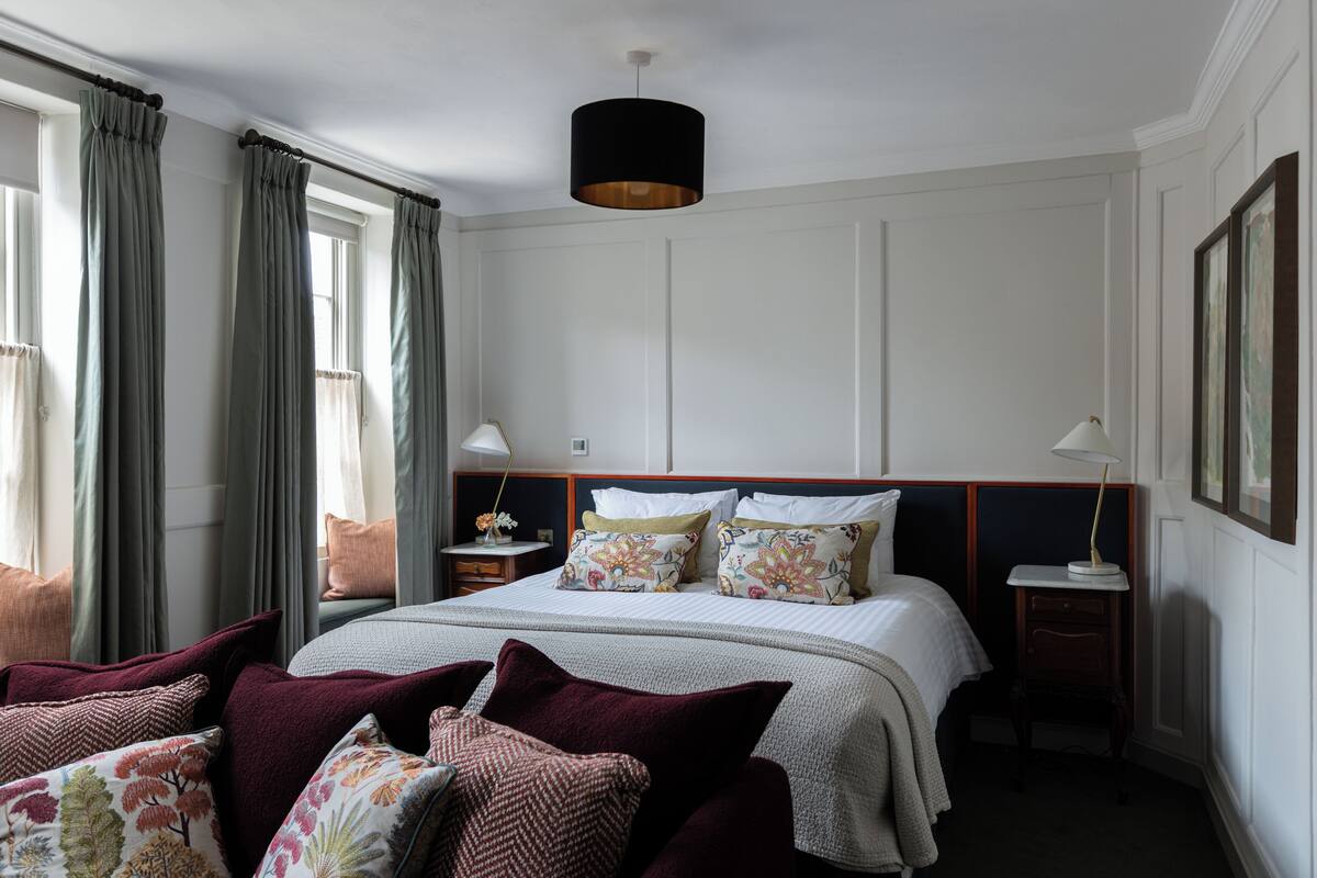 A hotel room with a large bed, two bedside tables, a hanging lamp, and a view of the city through the window.