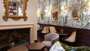 A room with a fireplace, a mirror, and a patterned wallpaper. There are chairs and a table with a vase of flowers. - White Hart Hotel (Lincoln)