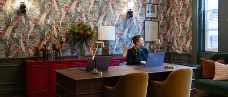 A room with a desk, two chairs, a laptop, a red cabinet, and a patterned wallpaper.