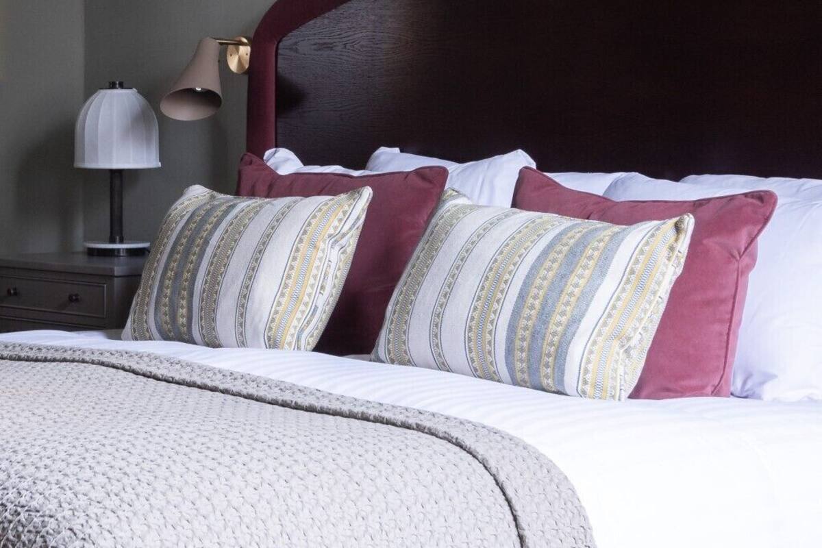 A neatly made bed with patterned pillows, a dark headboard, and a bedside lamp.