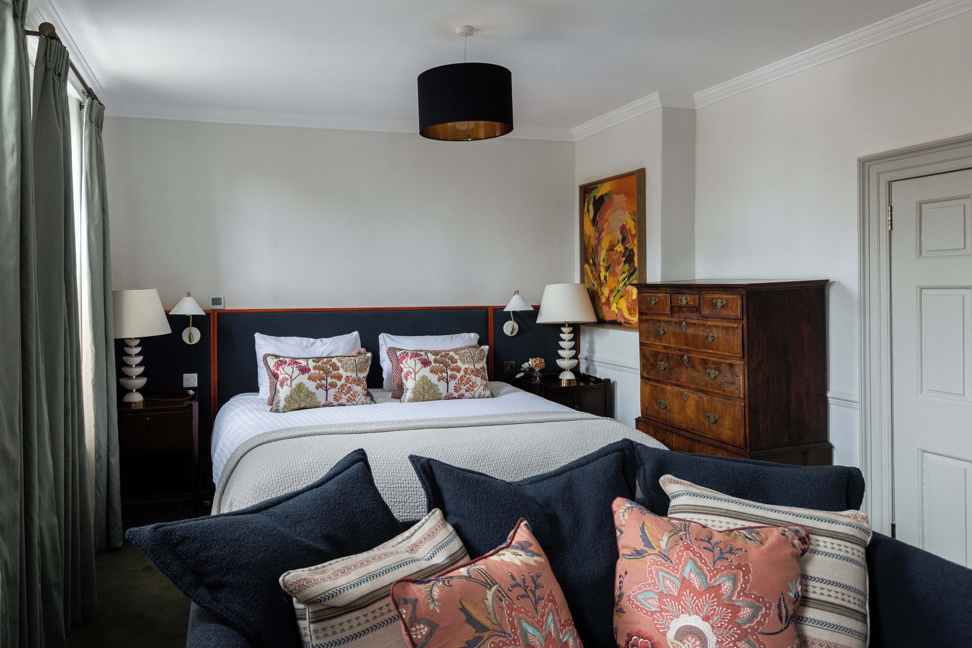 A neatly arranged bedroom with a large bed, two bedside tables with lamps, a wooden dresser, and a painting on the wall.