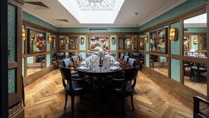 A dining room with a round table set for a meal, surrounded by chairs, with a skylight above and mirrored walls. - White Hart Hotel (Lincoln)