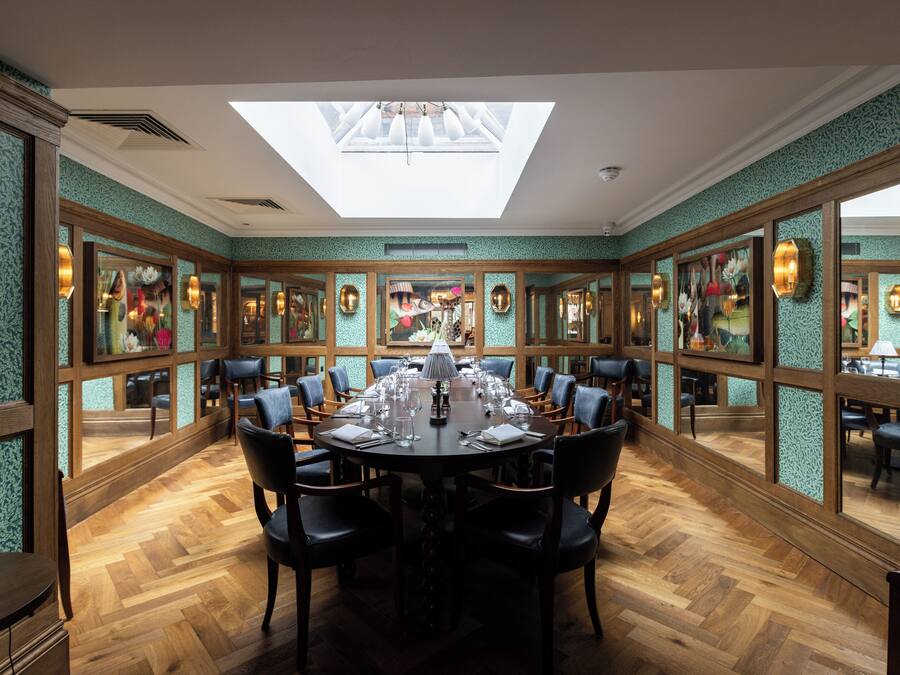 A dining room with a round table set for a meal, surrounded by chairs, with a skylight above and mirrored walls.
