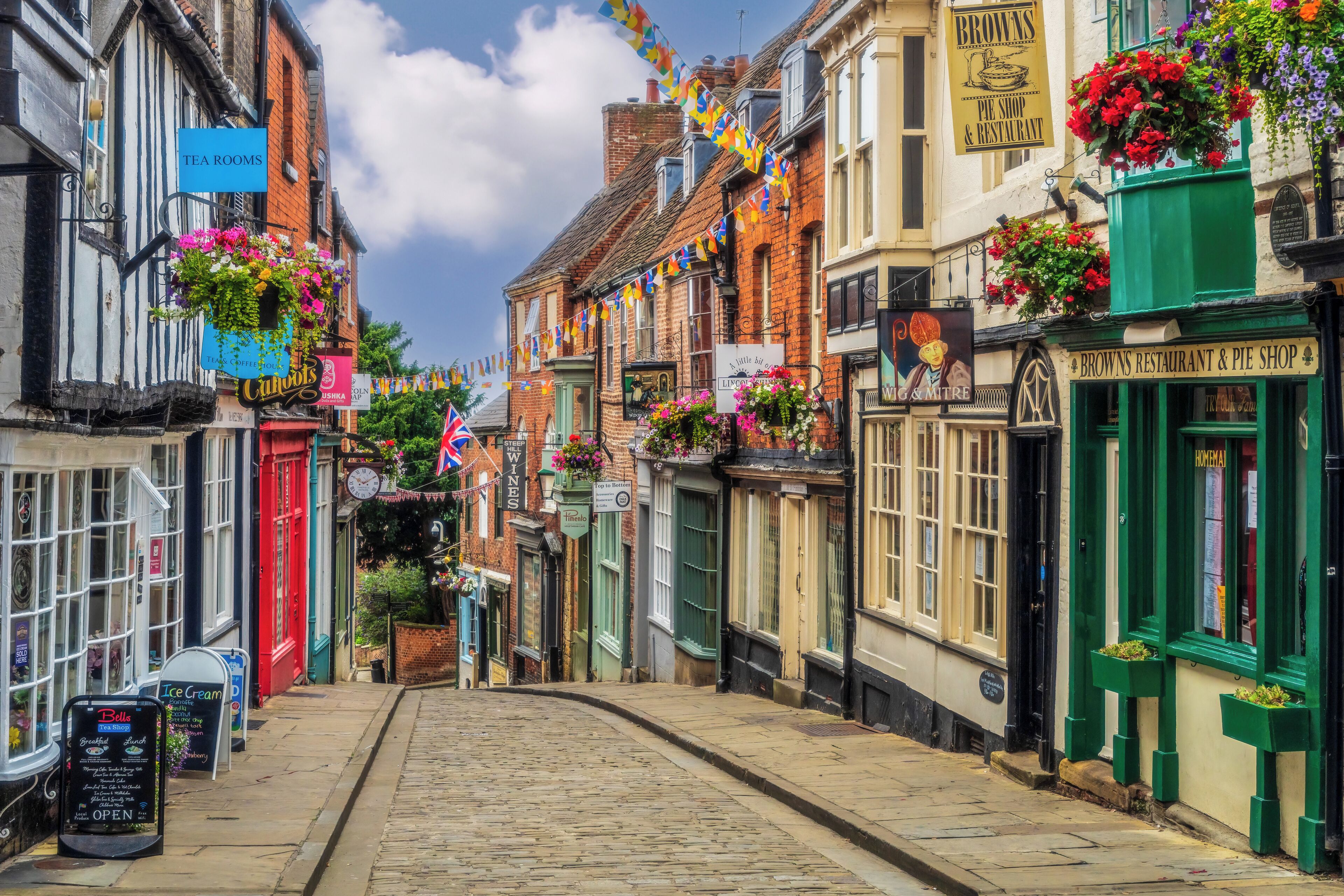 Una calle adoquinada bordeada de edificios tradicionales, algunos con macetas de flores y carteles de casas de té y restaurantes.