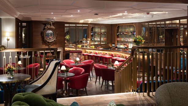 A bar area with red bar stools, a wooden bar counter, and a mirrored wall. - White Hart Hotel (Lincoln)