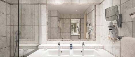 A modern bathroom with a large mirror, two sinks, a shower, and a hairdryer mounted on the wall.