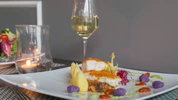 Une assiette blanche contenant un plat de poisson, un verre de vin blanc et une bougie sur une table.