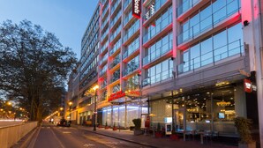 A modern hotel with a glass facade, outdoor seating, and a prominent neon sign. - Thon Hotel Bristol Stephanie (Brussels)