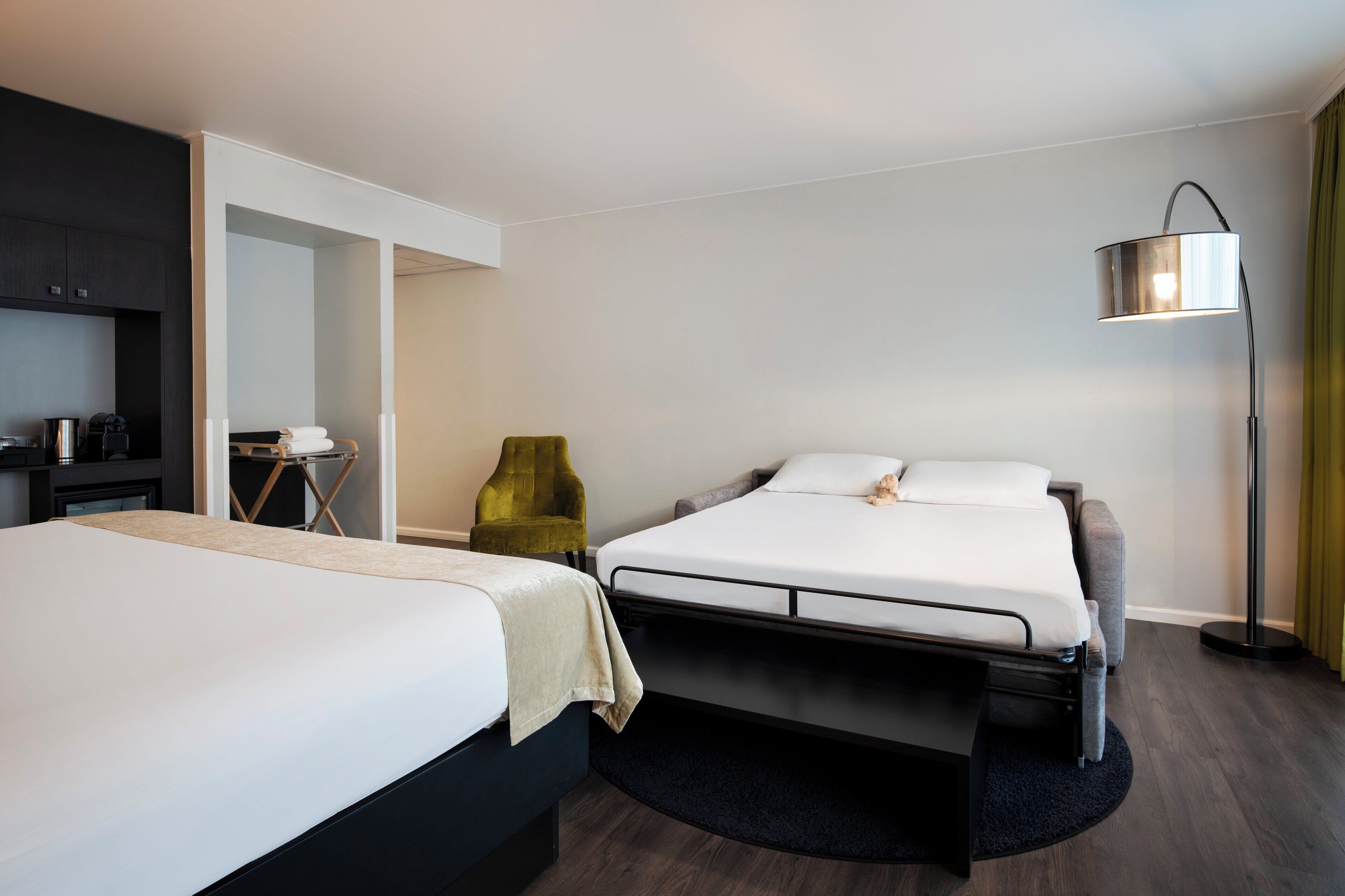 Une chambre d’hôtel avec deux lits, un bureau, une chaise et une lampe sur pied.