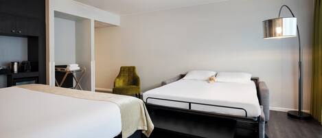 A hotel room with two beds, a desk, a chair, and a floor lamp.