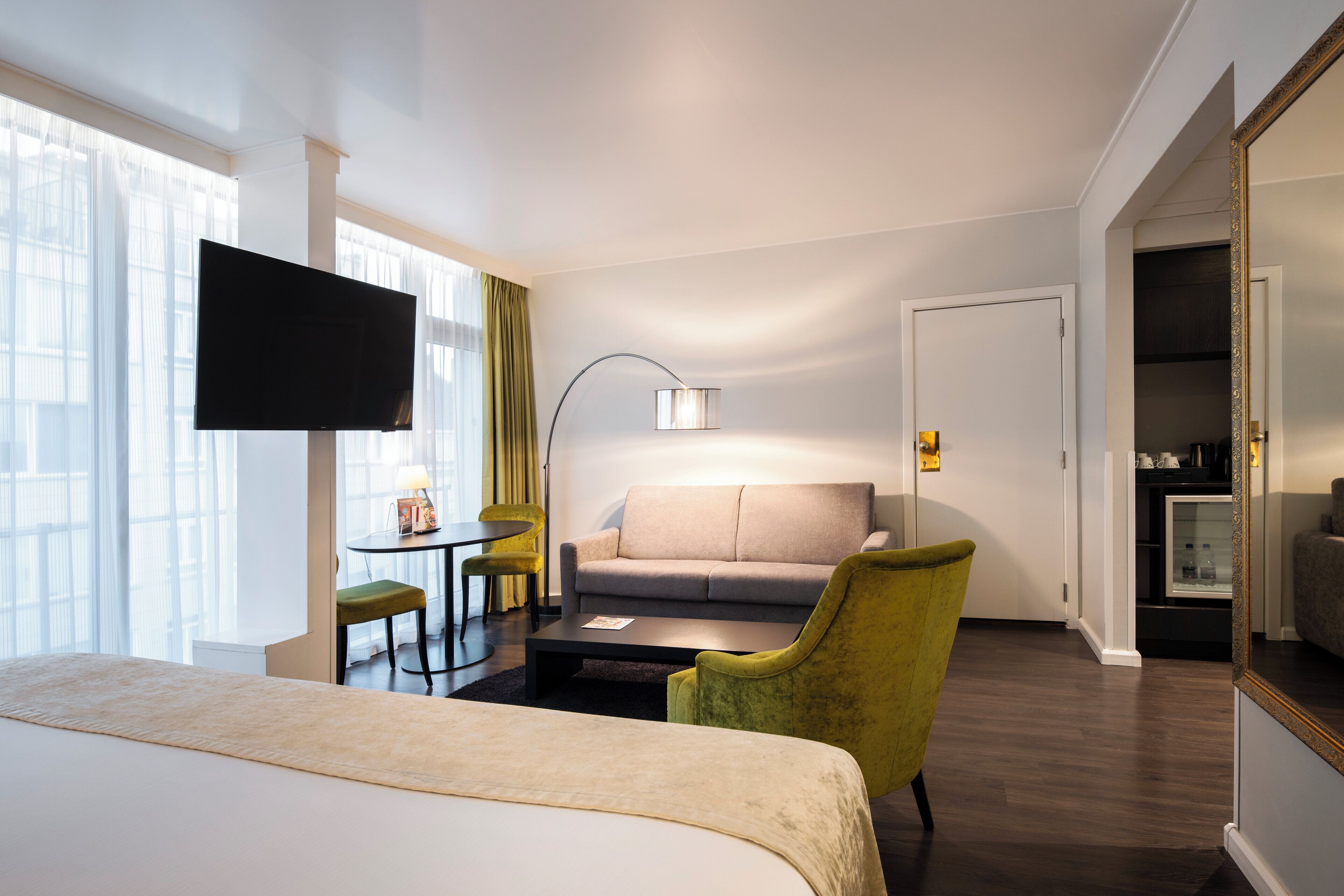 Une chambre d’hôtel comprenant un lit, un canapé, un bureau avec une lampe, une télévision et un miroir.