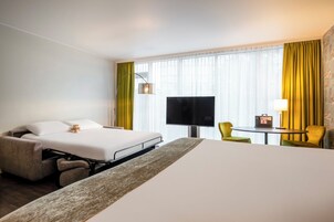 Una habitación de hotel con cama, escritorio, silla, televisor y ventana con cortinas.