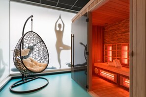 A room with a hanging chair, a sauna area with benches and heaters, and a glass partition. - Thon Hotel Bristol Stephanie (Brussels)