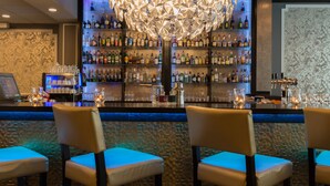 A bar area with a large chandelier, multiple shelves of bottles, and bar stools. - Thon Hotel Bristol Stephanie (Brussels)