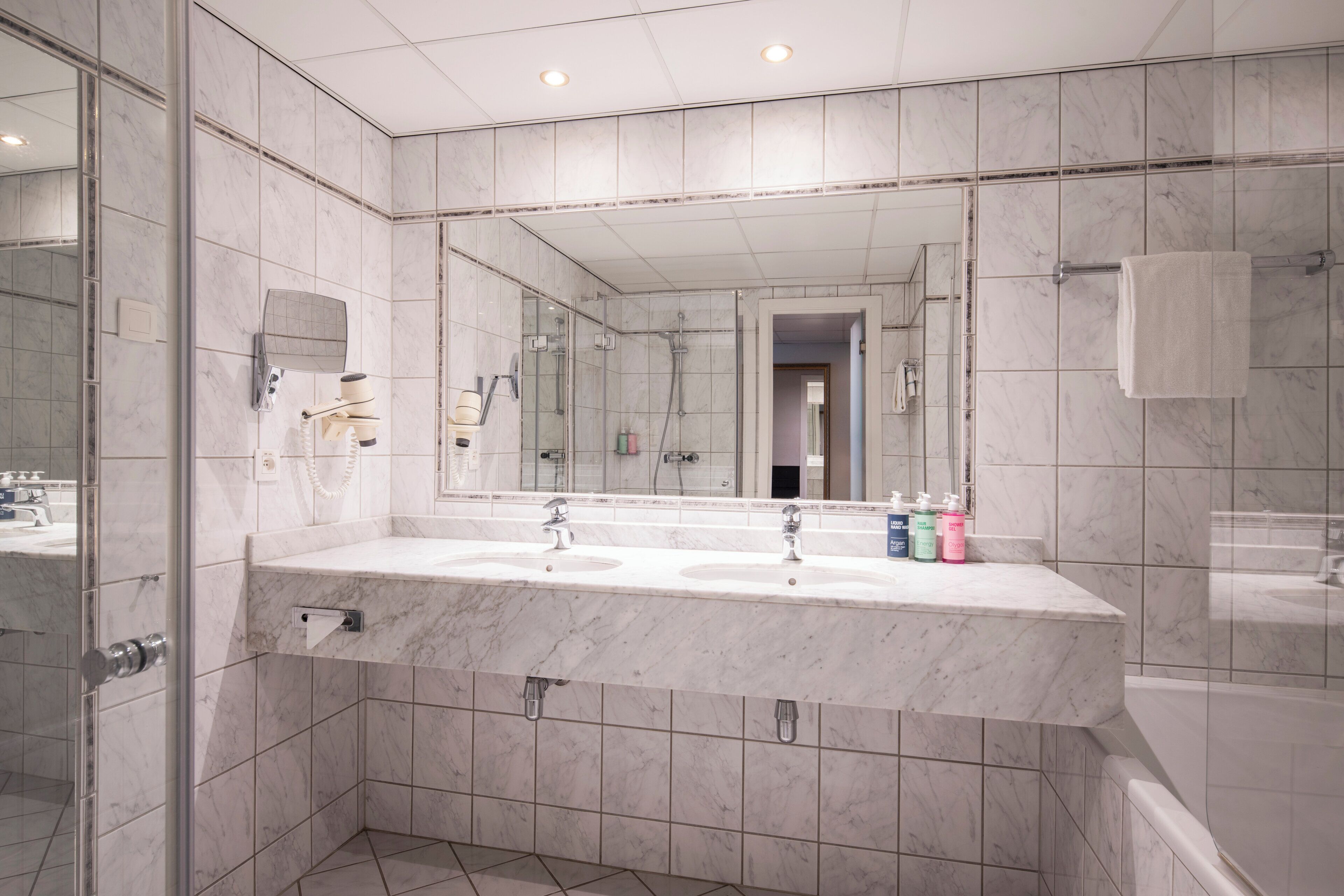 A modern bathroom with a large mirror, two sinks, and a bathtub.