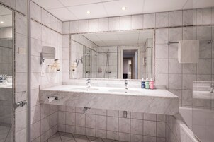 A modern bathroom with a large mirror, two sinks, and a bathtub.
