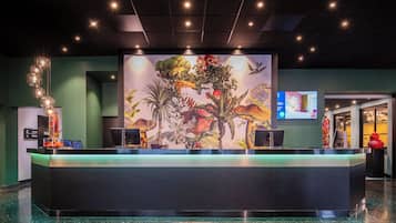 Un espace d’accueil comprenant une grande fresque murale, un comptoir d’accueil et un écran numérique.