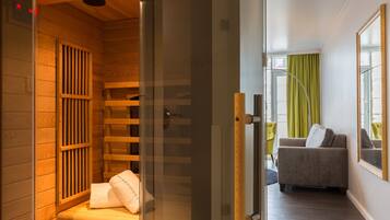 Un sauna aux murs en bois et à la porte en verre, donnant sur un espace de vie comprenant un canapé et des rideaux.
