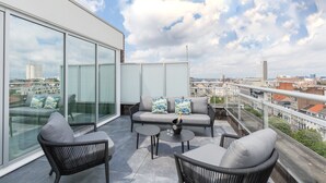 A modern balcony with a sofa, chairs, and a table, featuring a city view and large windows. - Thon Hotel Bristol Stephanie (Brussels)