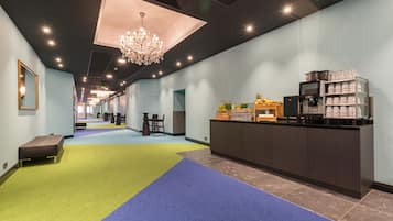A hotel lobby with a long corridor, a reception desk, a chandelier, and a coffee machine.