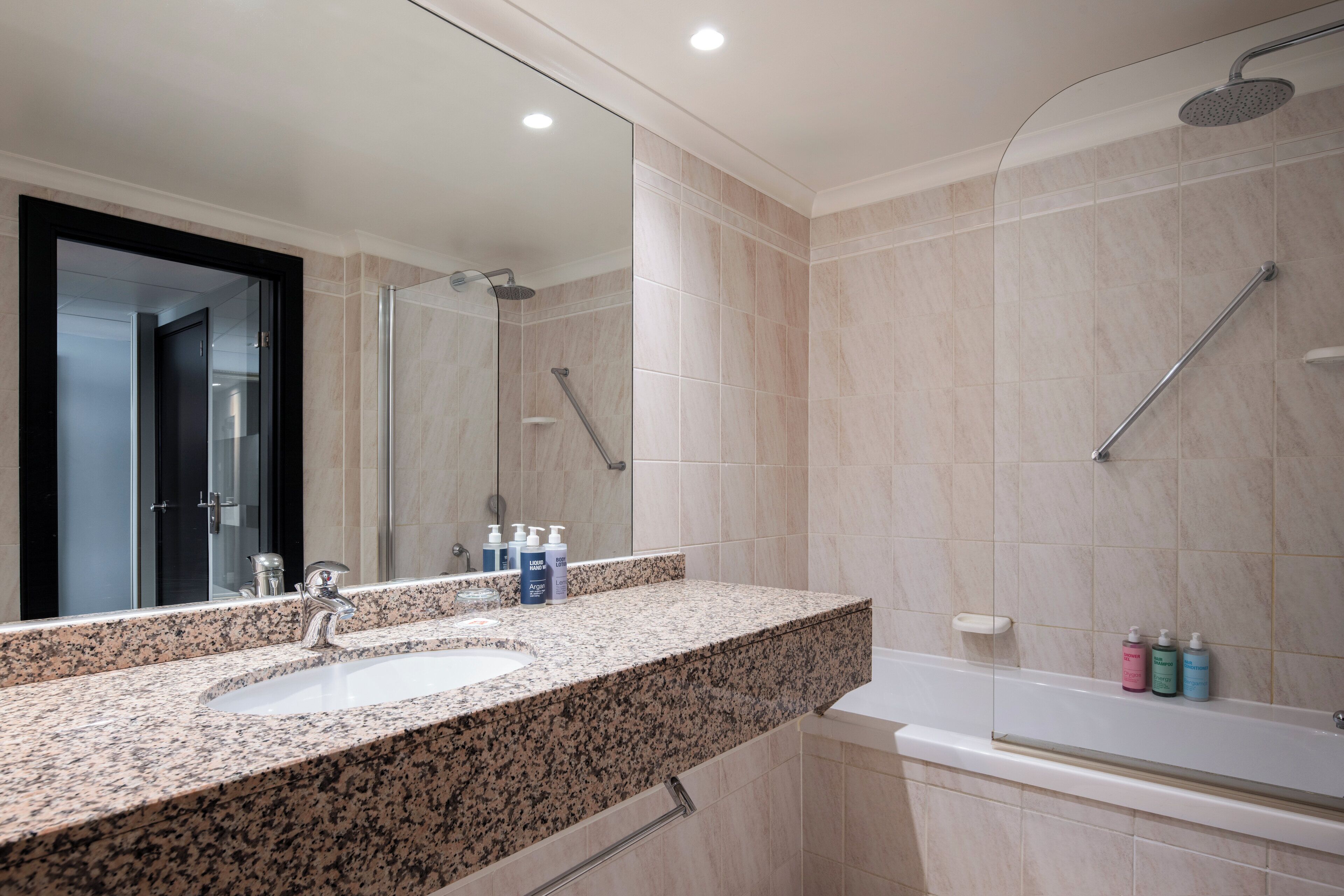 A modern bathroom with a granite countertop, a sink, a mirror, a shower, and a bathtub.