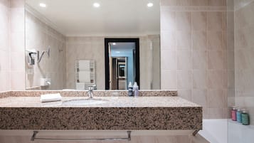 A modern bathroom with a granite countertop, a large mirror, a glass shower enclosure, and a visible towel rack.