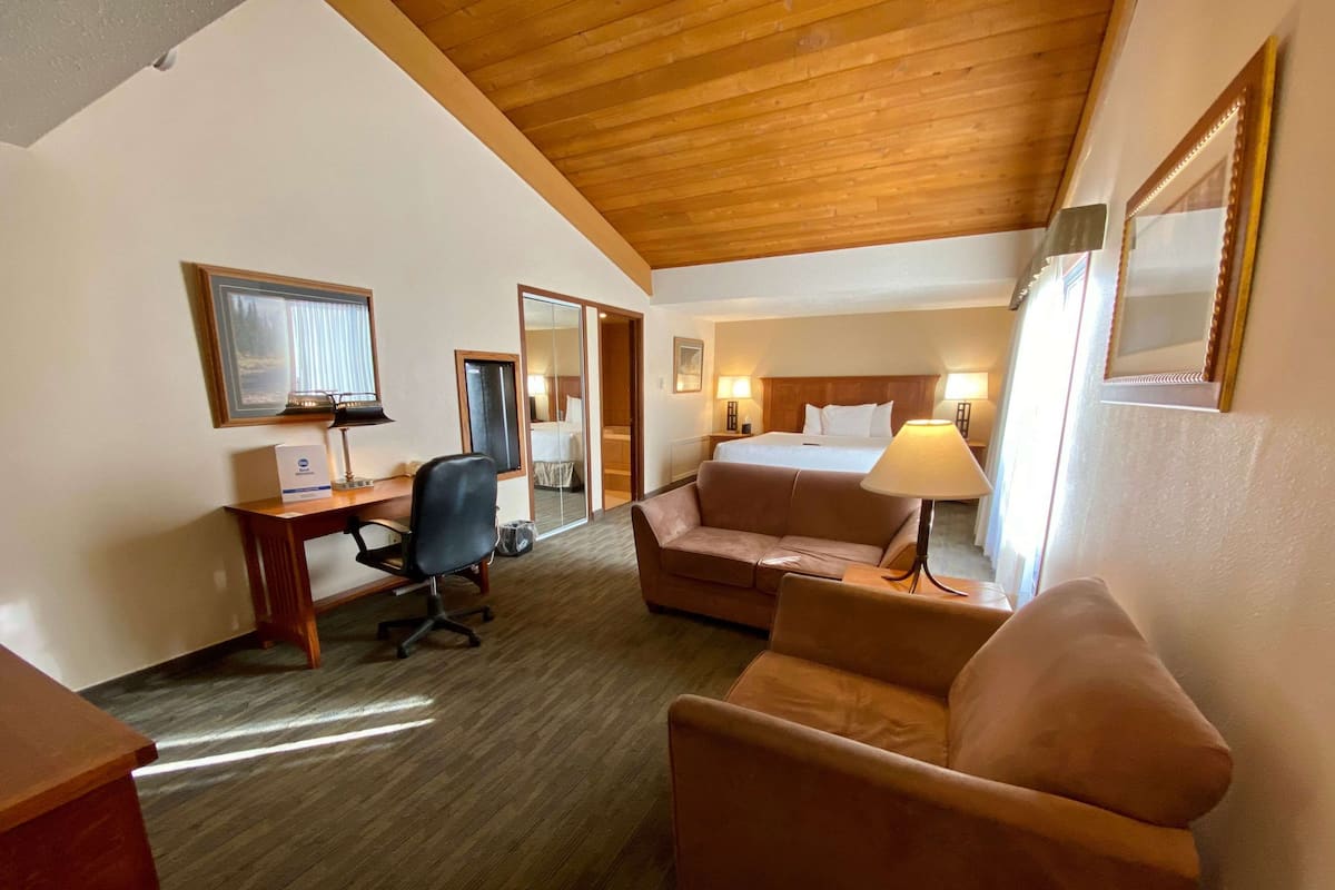 A hotel room with a wooden ceiling, a bed, a desk with a chair, a sofa, and a lamp.