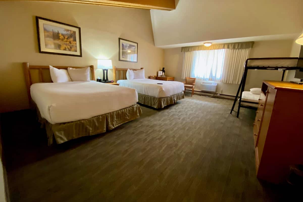 A hotel room with two beds, a desk, a chair, and two framed pictures on the wall.