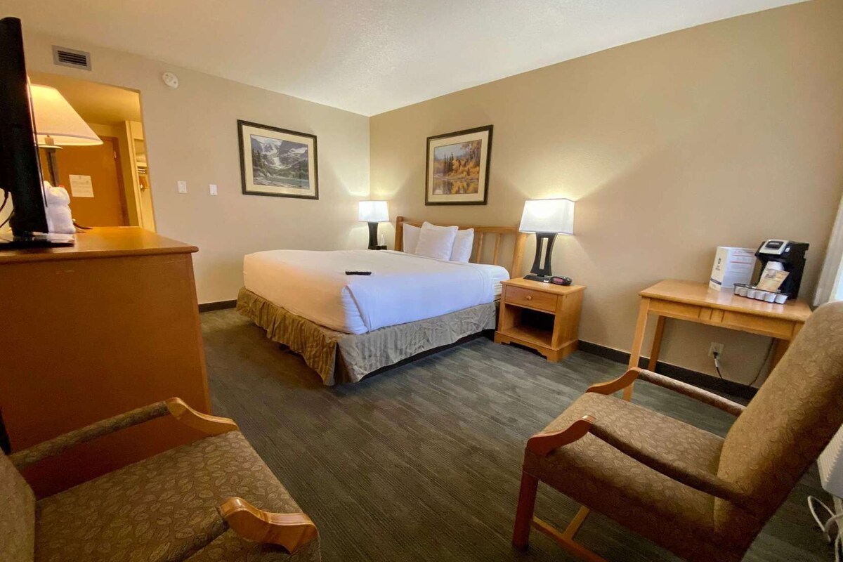 A hotel room with a bed, two bedside tables with lamps, a desk with a coffee maker, and two chairs.