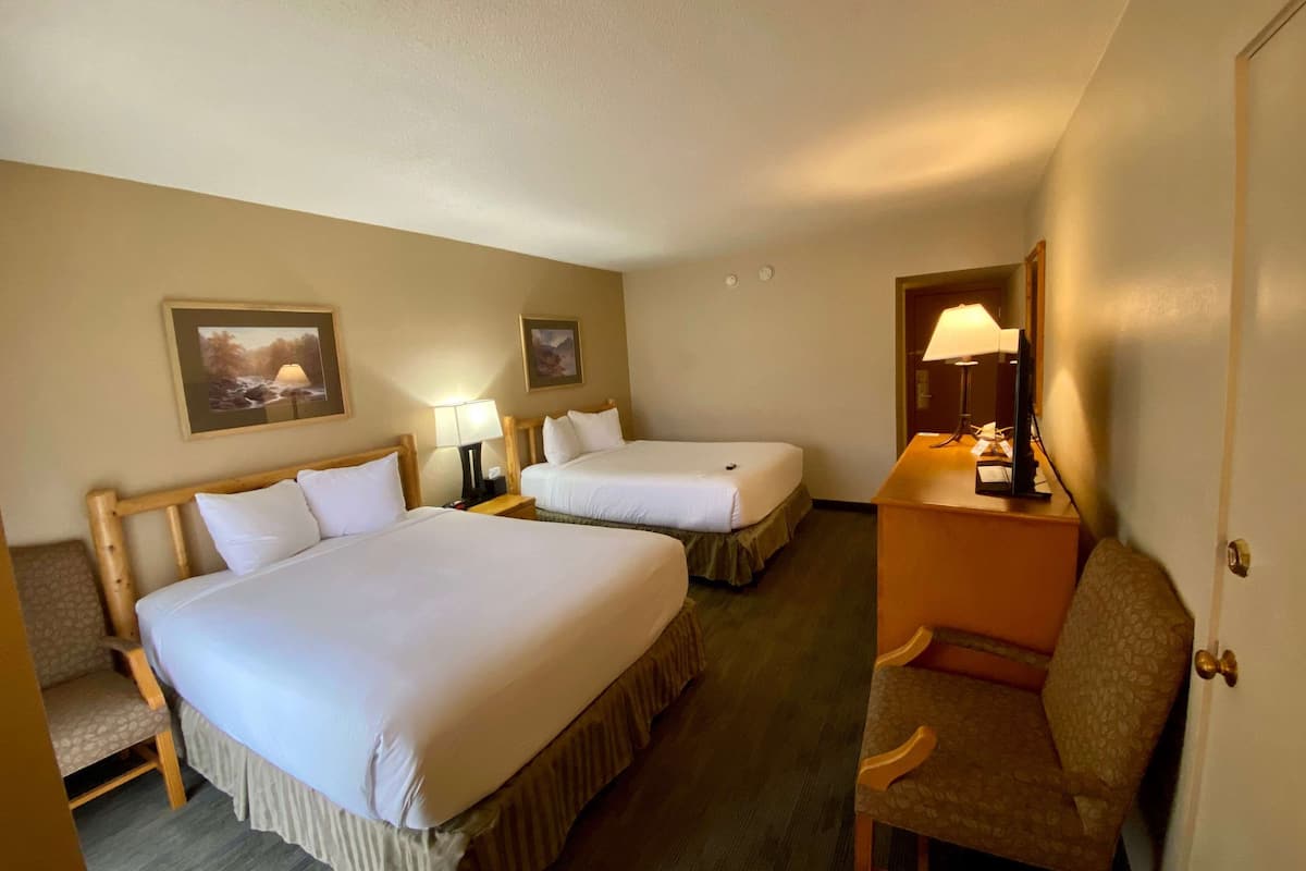 A hotel room with two beds, a desk with a lamp, a chair, and two wall-mounted lamps.