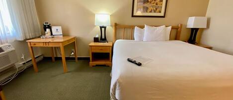 A hotel room with a large bed, a desk, a chair, a lamp, a painting on the wall, and a window with curtains.