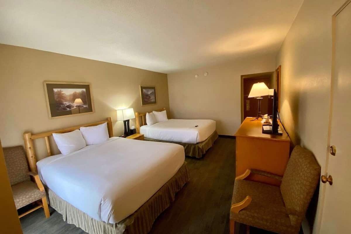A hotel room with two beds, a chair, a desk, and a lamp.