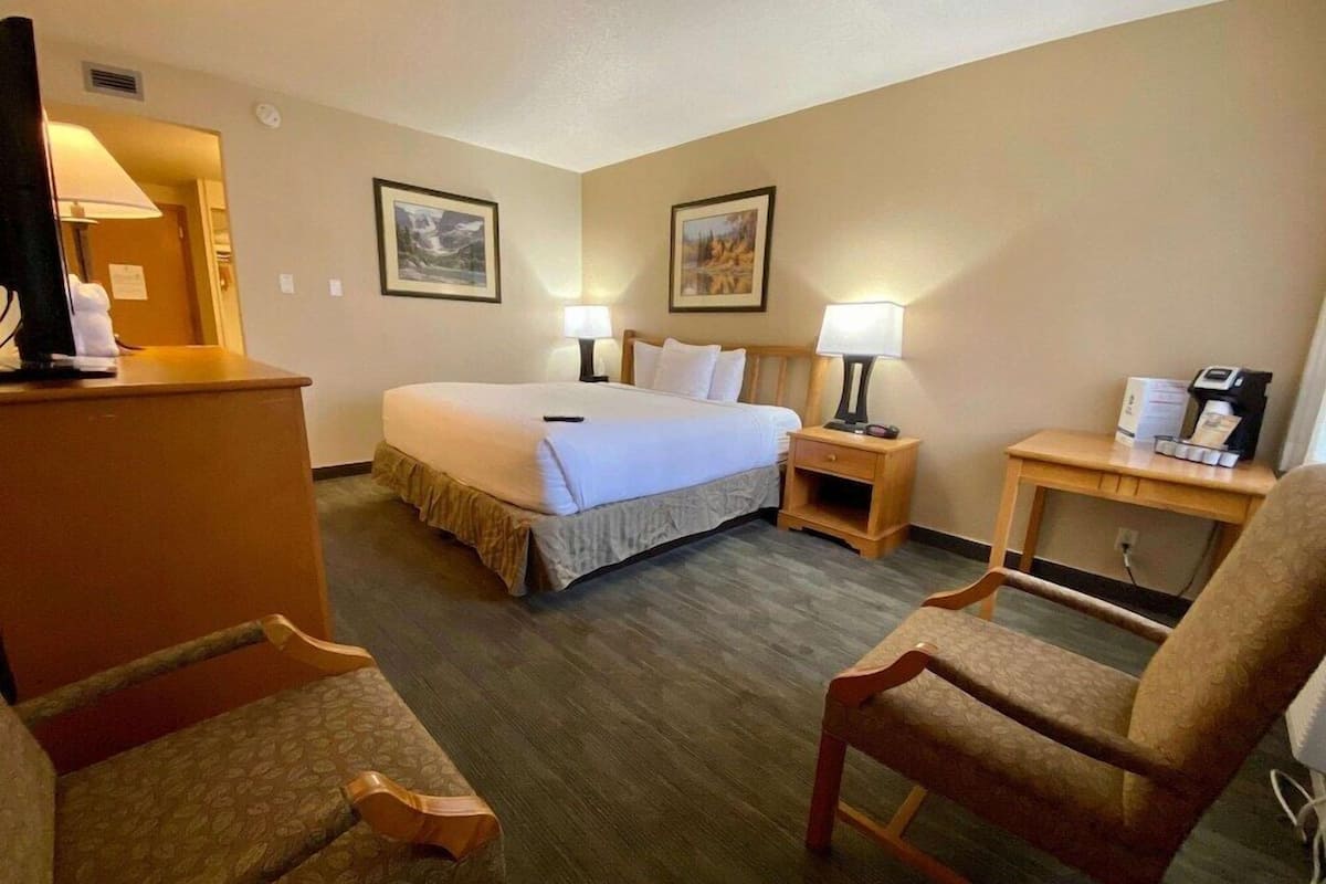 A hotel room with a bed, two bedside tables with lamps, a desk with a coffee maker, and two chairs.