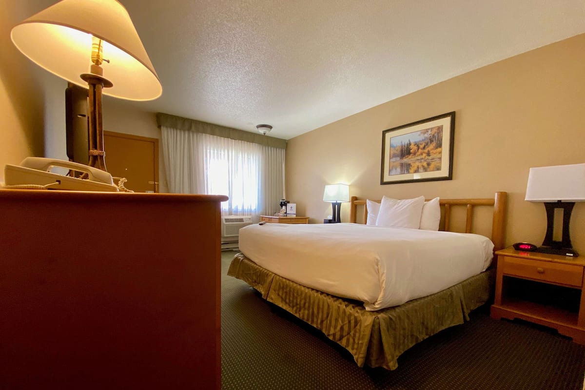 A hotel room with a large bed, a desk, a chair, a lamp, and a painting on the wall.