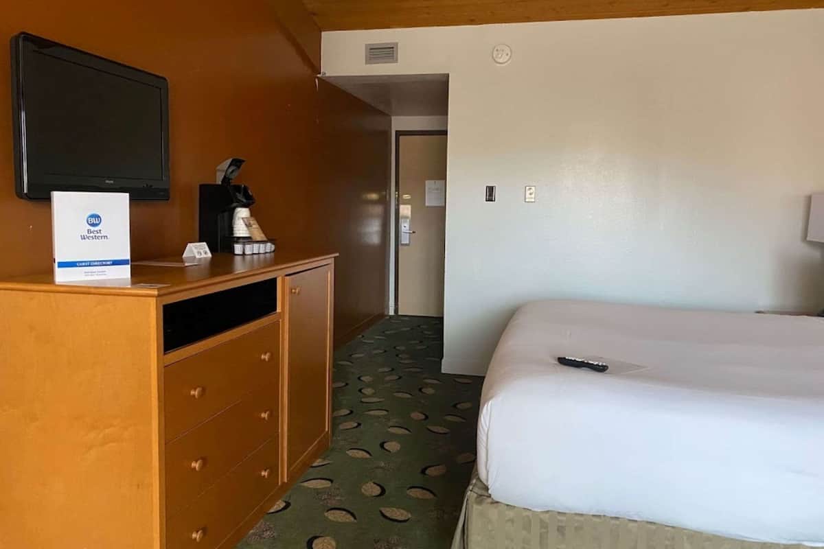 A hotel room with a bed, a desk with a coffee maker, a TV, and a sign for Best Western.