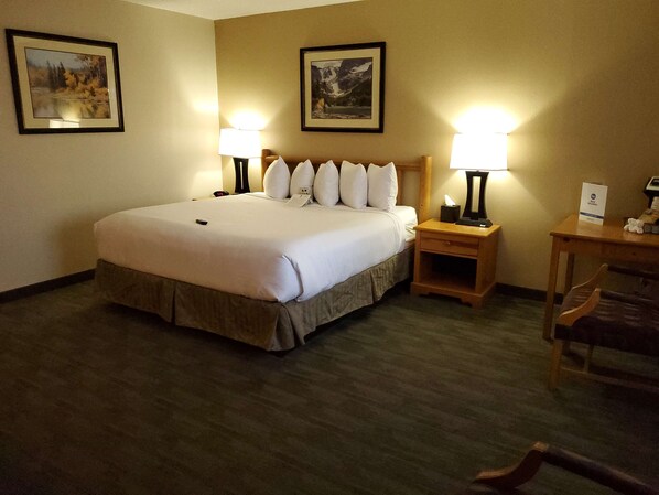A hotel room with a large bed, two bedside lamps, a wooden nightstand, a chair, and two framed pictures on the walls. - Best Western Sheridan Center (Sheridan)