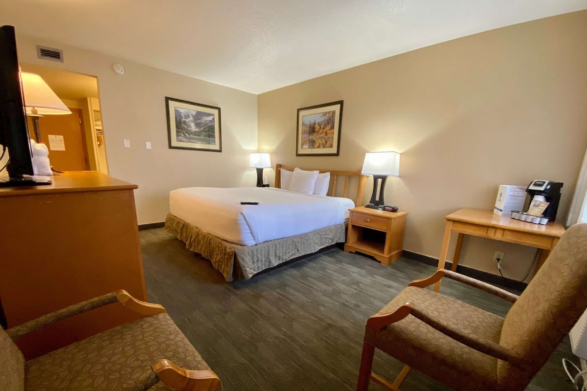 A hotel room with a bed, two bedside tables with lamps, a desk with a coffee maker, and two chairs.