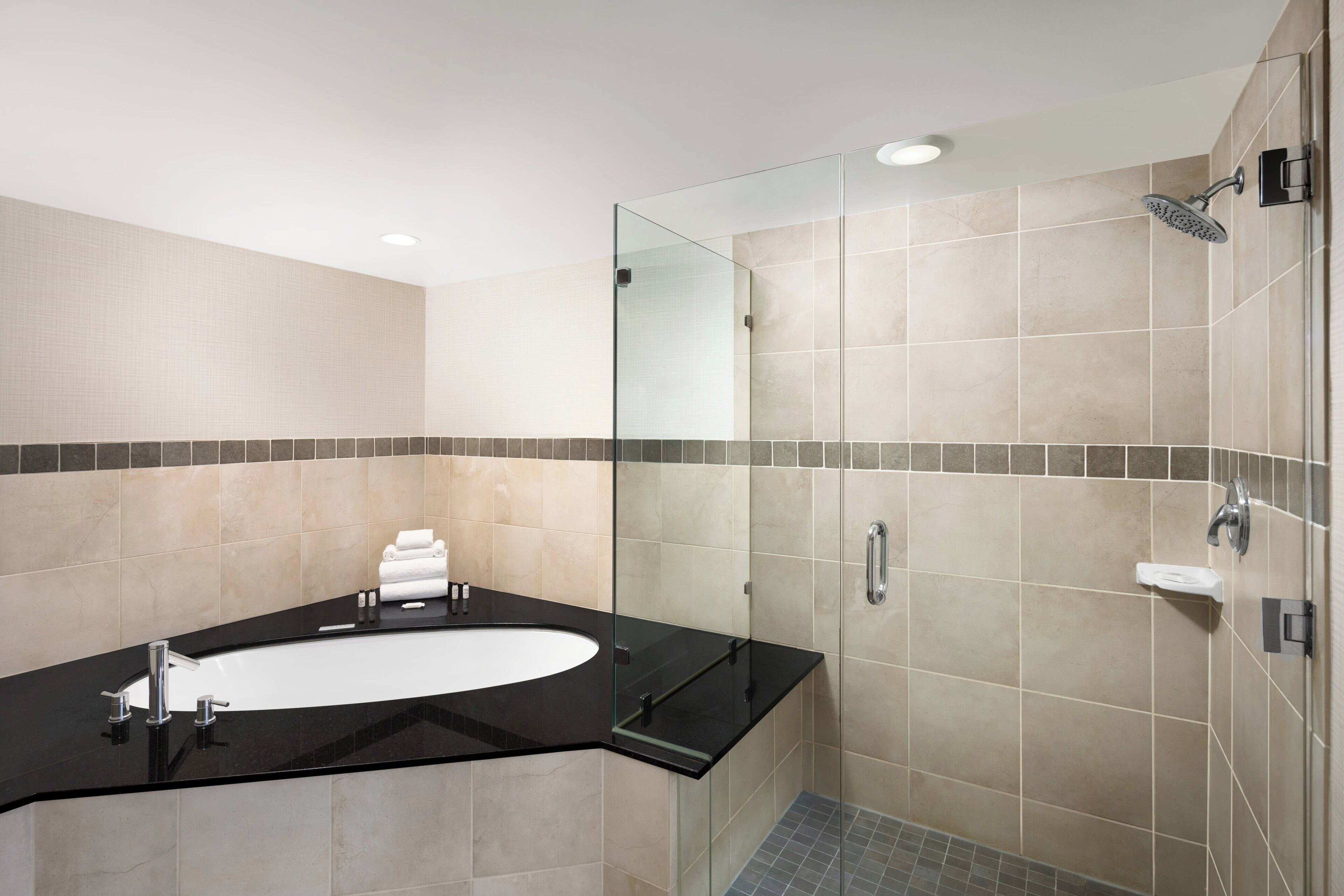 A modern bathroom with a black sink, a glass shower enclosure, and beige tiled walls.