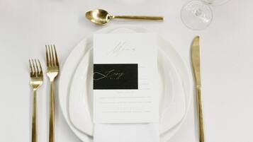 A table setting with a menu, gold cutlery, and wine glasses.