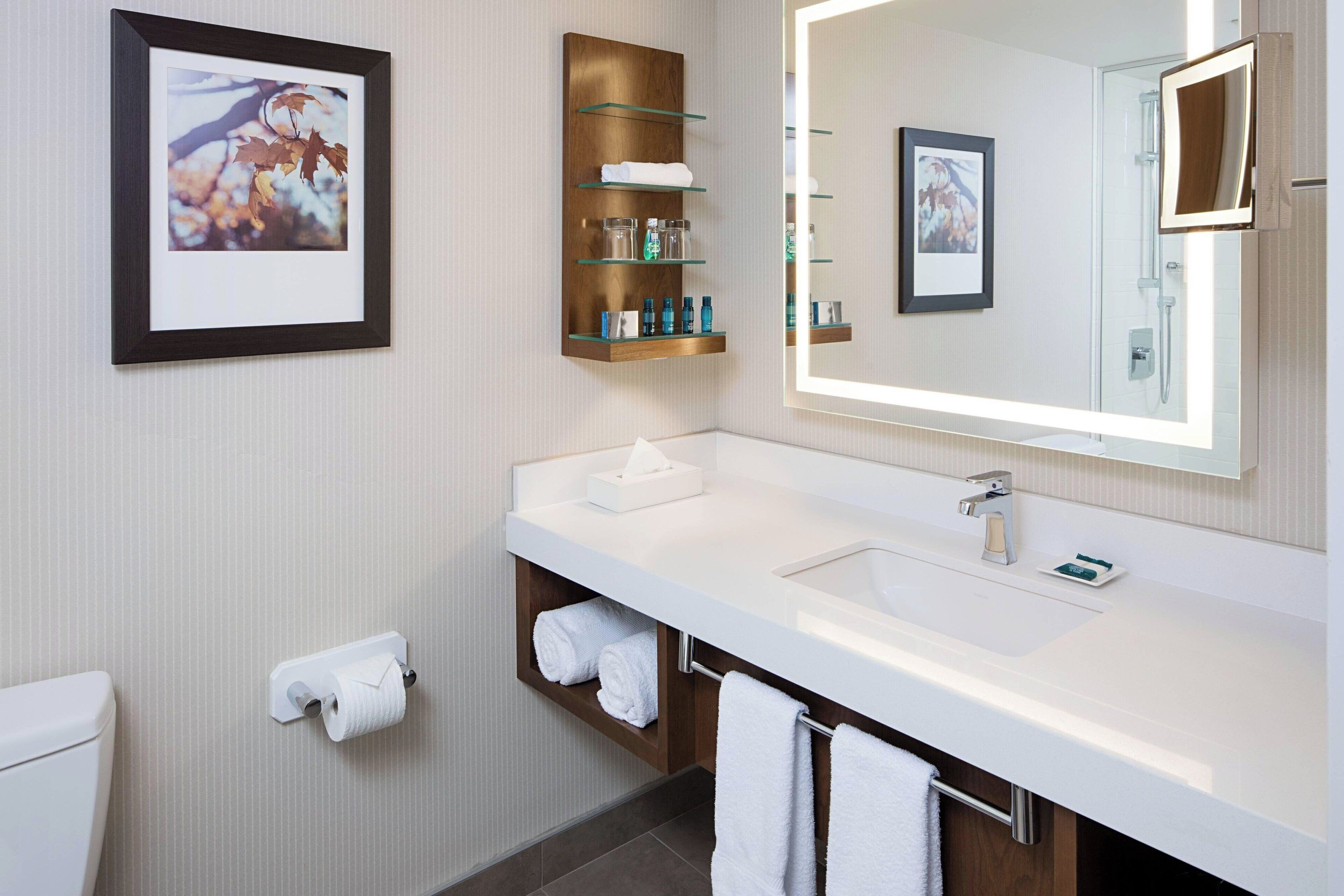 Un baño moderno con un lavamanos blanco, un espejo grande, un cuadro enmarcado y un perchero para toallas.