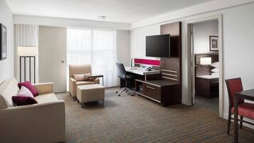 A hotel room with a bed, a desk, a chair, a TV, and a window with curtains.