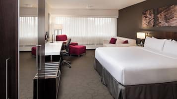 Habitación de hotel con una cama grande, un escritorio con silla, un sofá rojo y un ventanal con cortinas.