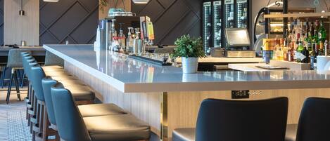 A modern bar area with a long counter, multiple bar stools, and a television screen.