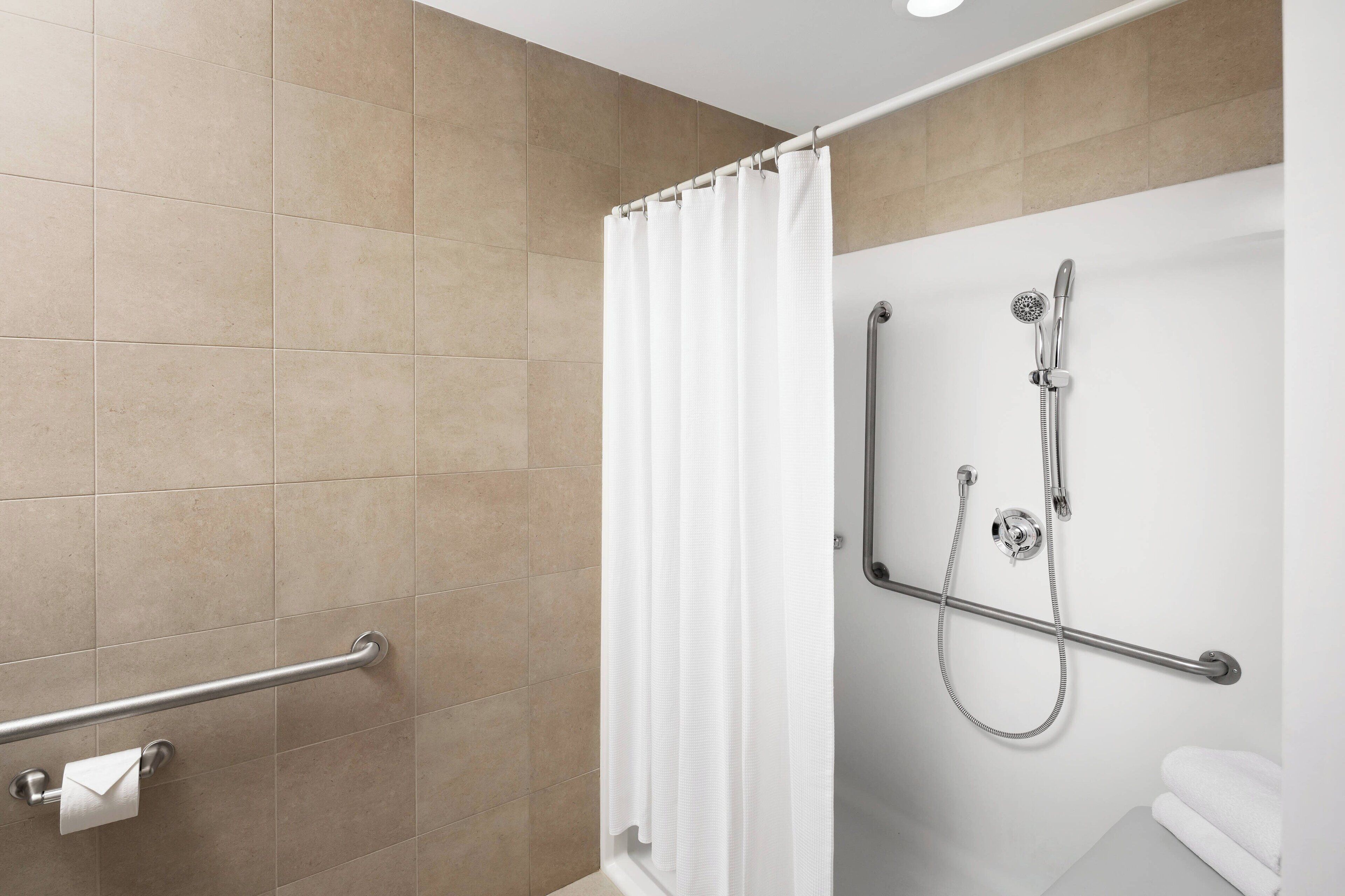 Un baño con ducha, barra de apoyo y toallero.
