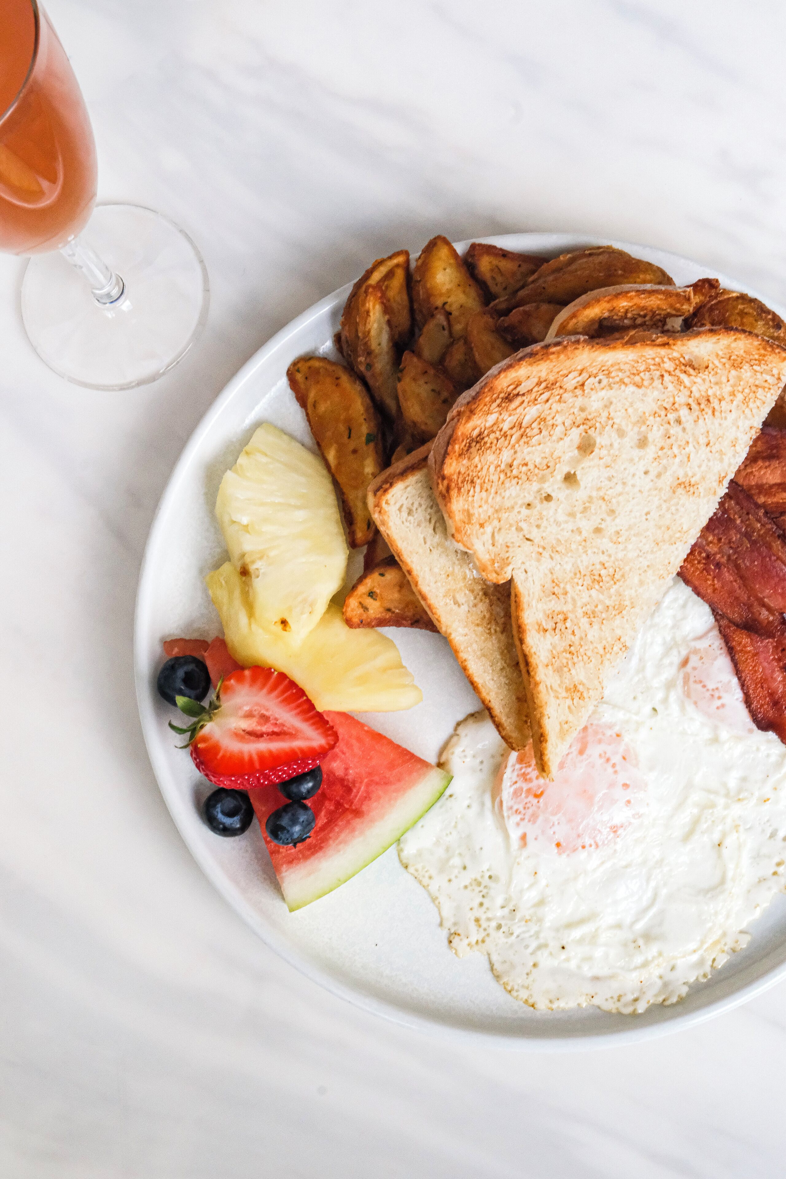 Un plato de comida para el desayuno que incluye tostadas, huevos, tocino, papas y fruta.