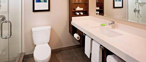 Un baño moderno con inodoro, ducha, lavabo con espejo y estantes con artículos de aseo.