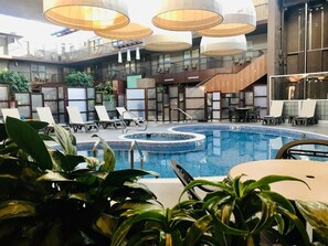 Zona de piscina de hotel con sillones de descanso, una bañera de hidromasaje circular e iluminación moderna.