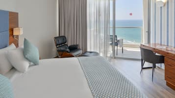 A hotel room with a bed, a desk, a chair, and a view of the ocean.