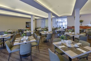 A spacious dining area with multiple tables and chairs, equipped with place settings and potted plants. - Sharon Hotel Herzliya (Herzliya)